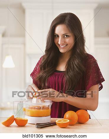 Stock Photography - Mixed race woman making fresh orange juice. Fotosearch