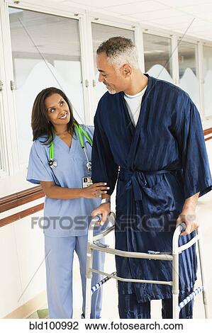 Stock Image - Nurse helping patient use walker in hospital. Fotosearch