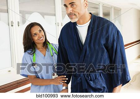 Stock Image - Nurse helping patient walk in hospital. Fotosearch