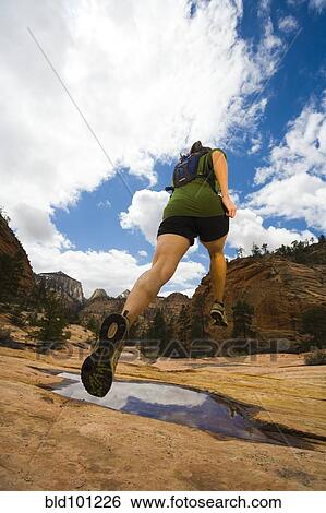 Stock Photograph - Persian woman jumping over canyon puddle. Fotosearch