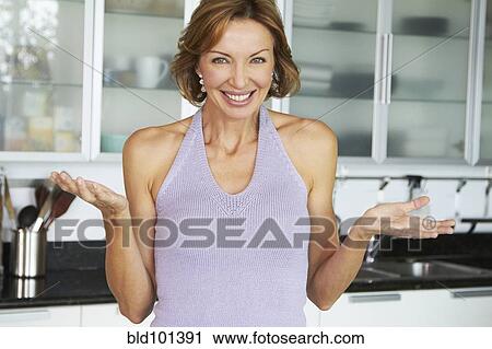 Stock Image - Smiling Caucasian woman standing in kitchen. Fotosearch