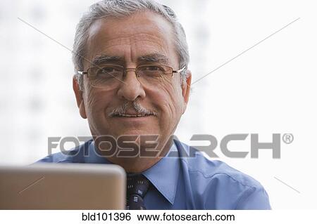 Stock Photograph - Smiling Hispanic businessman using laptop. Fotosearch