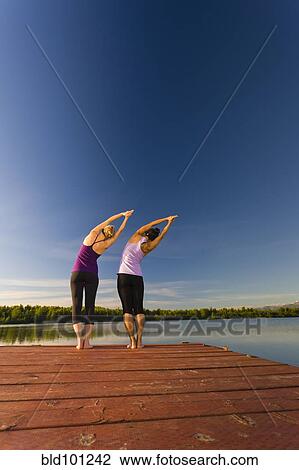 Stock Image - Woman practicing yoga on lake pier. Fotosearch