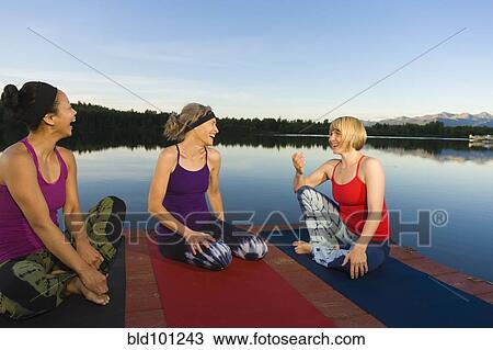 Stock Image - Woman practicing yoga on lake pier. Fotosearch