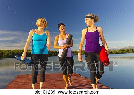 Stock Photo - Women carrying yoga mats on lake pier. Fotosearch