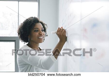 Picture - African American businesswoman writing on whiteboard in meeting. Fotosearch