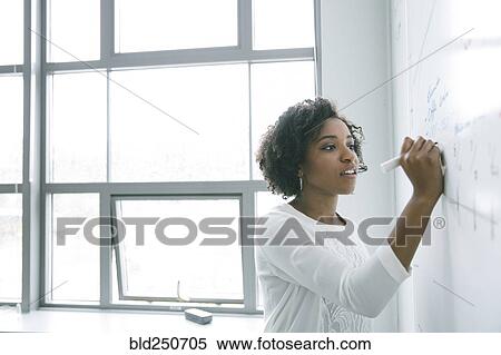 Stock Photography - African American businesswoman writing on whiteboard in meeting. Fotosearch