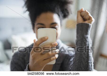 Stock Photograph - African American woman celebrating while texting on cell phone. Fotosearch