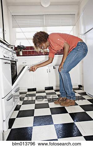 Stock Photograph - African American woman looking in oven. Fotosearch