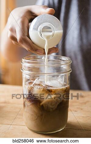 Stock Photograph - African American woman pouring milk into jar of coffee. Fotosearch