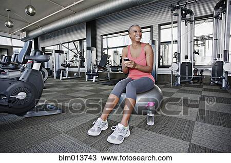 Stock Image - African American woman text messaging on cell phone in health club. Fotosearch