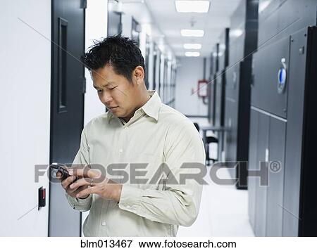 Stock Photo - Asian businessman using cell phone in server room. Fotosearch