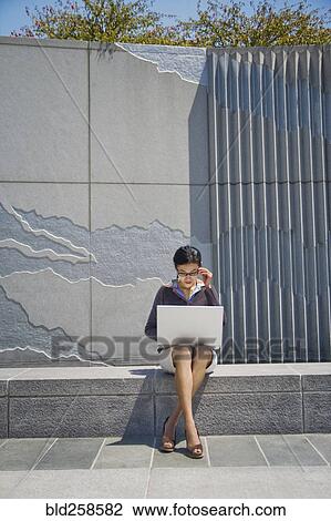 Asian businesswoman sitting on concrete wall using laptop View Large Photo Image Stock Image - Asian businesswoman sitting on concrete wall using laptop. Fotosearch