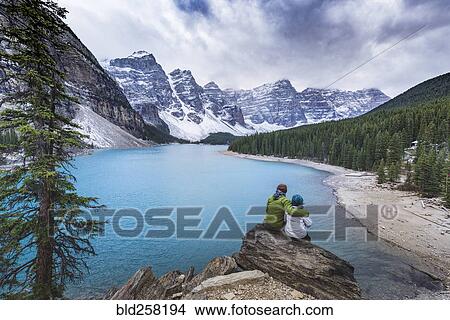 Asian couple sitting on rock admiring scenic view of mountain lake View Large Photo Image Picture - Asian couple sitting on rock admiring scenic view of mountain lake. Fotosearch