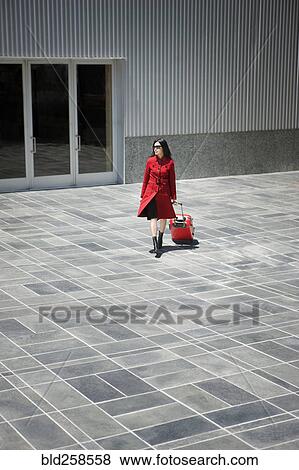 Asian woman pulling rolling suitcase near building View Large Photo Image Stock Photo - Asian woman pulling rolling suitcase near building. Fotosearch