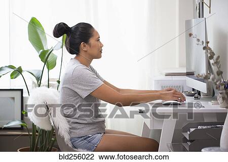 Stock Image - Asian woman using computer in home office. Fotosearch