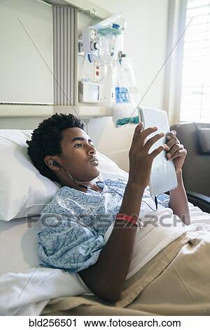 Stock Image - Black boy in hospital bed listening to digital tablet. Fotosearch