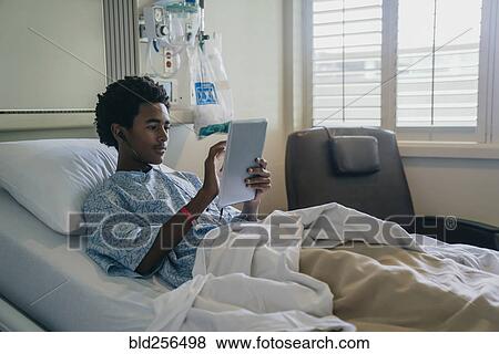 Black boy in hospital bed listening to digital tablet View Large Photo Image Stock Photo - Black boy in hospital bed listening to digital tablet. Fotosearch
