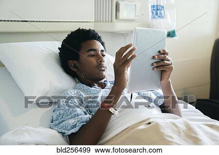 Stock Photo - Black boy in hospital bed listening to digital tablet. Fotosearch