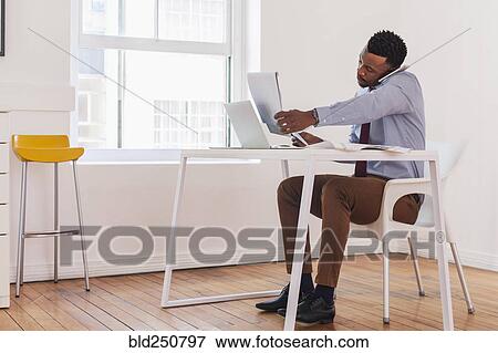 Stock Photo - Black businessman talking on cell phone and reading notepad. Fotosearch