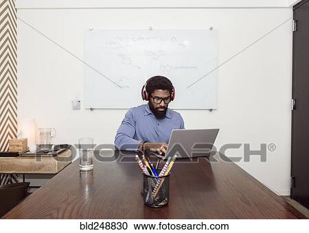 Black businessman wearing headphones using laptop View Large Photo Image Stock Image - Black businessman wearing headphones using laptop. Fotosearch