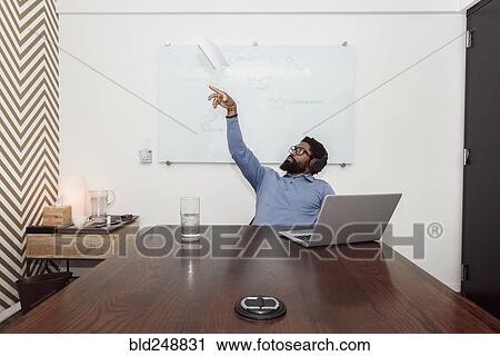 Stock Image - Black businessman wearing headphones throwing paper airplane. Fotosearch