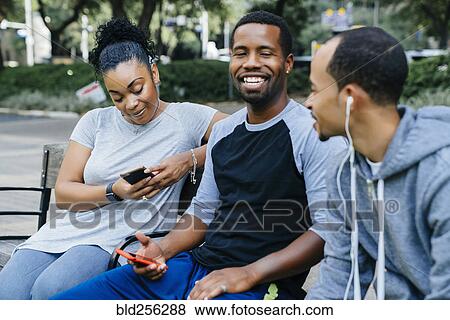 Black friends sitting on bench holding cell phones View Large Photo Image Stock Photo - Black friends sitting on bench holding cell phones. Fotosearch