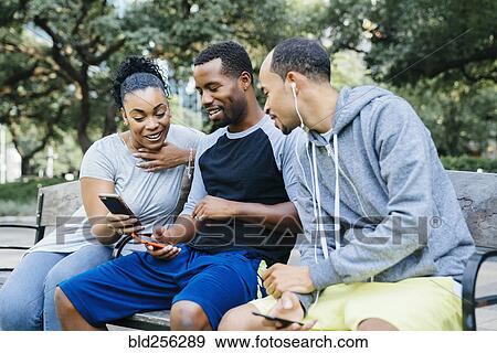 Black friends sitting on bench texting on cell phones View Large Photo Image Stock Photo - Black friends sitting on bench texting on cell phones. Fotosearch
