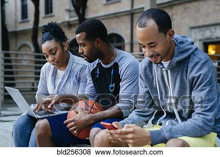 Stock Photo - Black friends using laptop and cell phone. Fotosearch