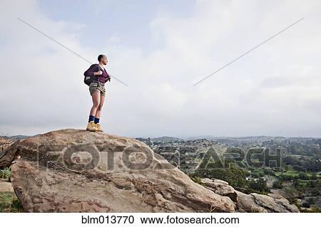 Stock Image - Black hiker standing on rock in remote area. Fotosearch