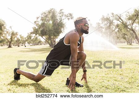 Picture - Black man crouching in park stretching legs. Fotosearch