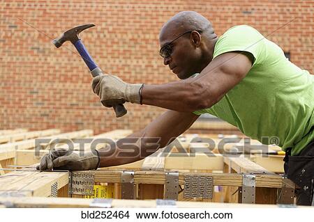 Picture - Black man hammering nail at construction site. Fotosearch