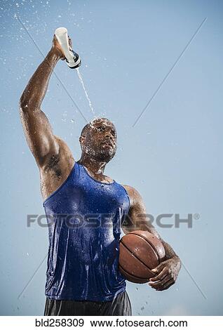 Stock Photo - Black man holding basketball cooling off with water bottle. Fotosearch