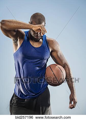 Stock Photograph - Black man holding basketball wiping sweat off forehead. Fotosearch