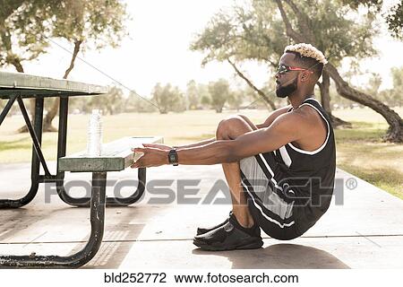 Stock Image - Black man holding picnic table in park stretching arms. Fotosearch