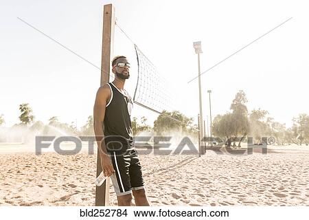 Picture - Black man leaning on beach volleyball net. Fotosearch