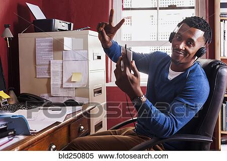 Stock Photography - Black man listening to cell phone with headphones. Fotosearch