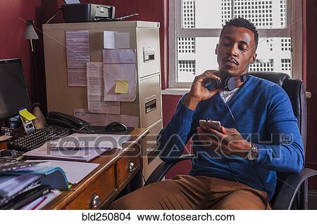 Black man reading cell phone and holding headphones View Large Photo Image Picture - Black man reading cell phone and holding headphones. Fotosearch