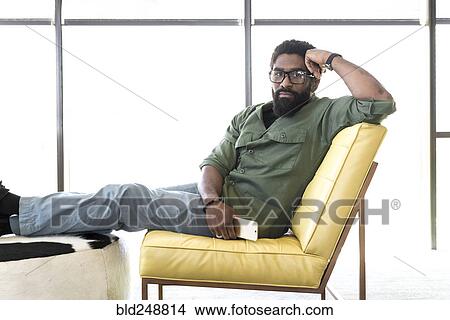 Picture - Black man sitting in chair holding cell phone. Fotosearch