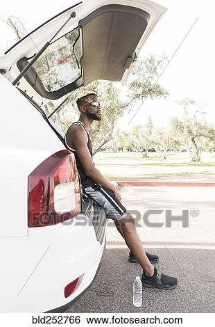 Stock Photograph - Black man sitting on car hatchback. Fotosearch