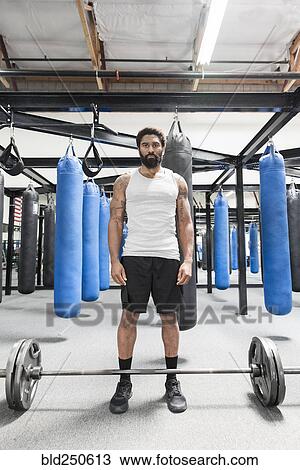 Stock Image - Black man standing near barbell in gymnasium. Fotosearch