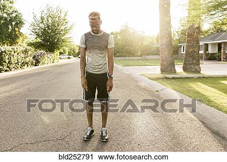 Stock Image - Black man standing on street in the neighborhood looking down. Fotosearch