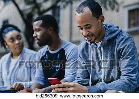 Stock Photo - Black man texting on cell phone near friends. Fotosearch