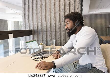 Stock Photo - Black man wearing headset using laptop. Fotosearch