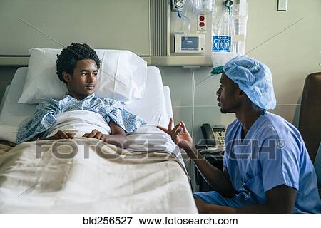 Stock Photo - Black nurse talking to boy in hospital bed. Fotosearch