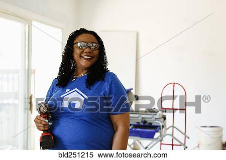 Stock Photography - Black volunteer woman holding drill. Fotosearch