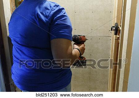 Stock Image - Black woman holding drill near wall. Fotosearch
