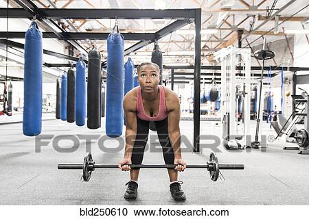 Stock Image - Black woman lifting barbell in gymnasium. Fotosearch
