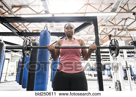 Stock Image - Black woman lifting barbell in gymnasium. Fotosearch