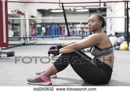 Stock Image - Black woman sitting on floor in boxing ring. Fotosearch